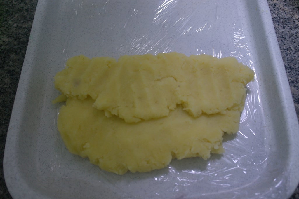 在操作台上铺保鲜膜，然后将土豆面团铺在上面